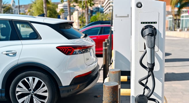 Allianz güvencesiyle elektrikli araç şarj istasyonunda park halindeki beyaz SUV otomobil.