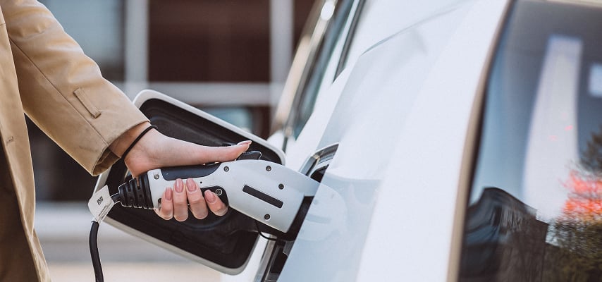 Beyaz elektrikli aracını şarj istasyonuna bağlayan sürücü. Allianz elektrikli araç kaskosu güvencesi.