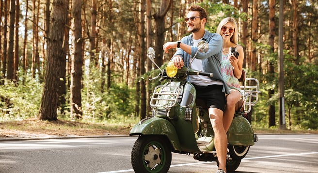 Orman yolunda yeşil scooter kullanan mutlu çift. Güvenli seyahat ve motosiklet sigortası konsepti.