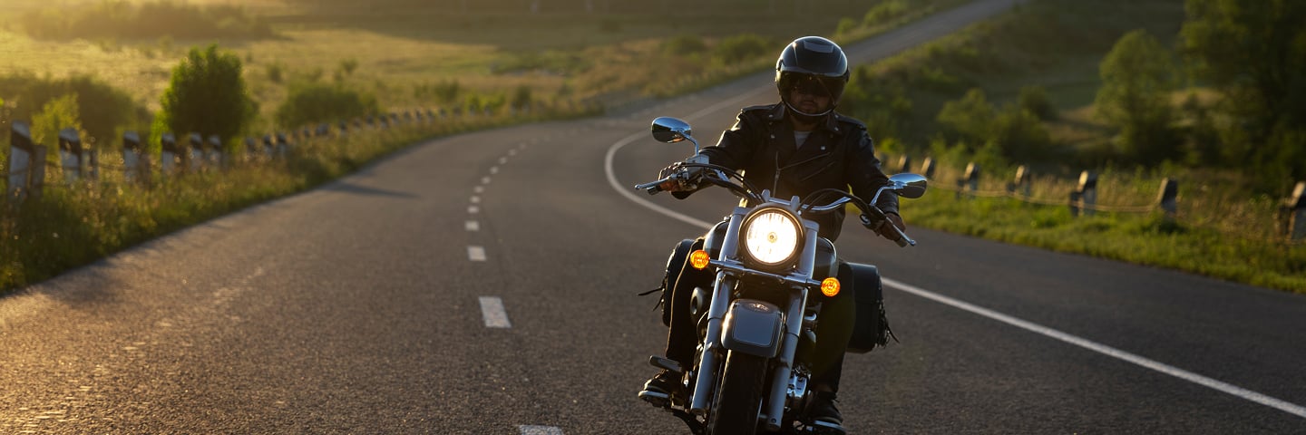 Allianz güvencesiyle gün batımında yolda güvenle motosiklet süren kasklı sürücü.