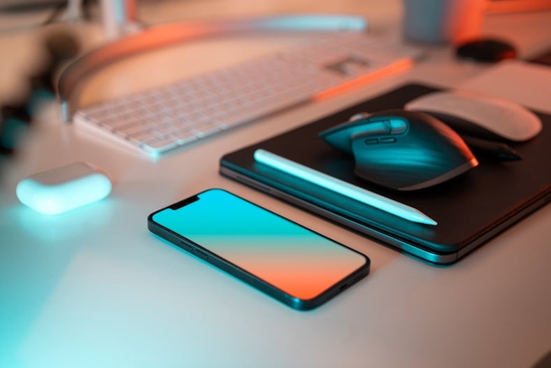 Neon ışıklı masada akıllı telefon, tablet ve bilgisayar aksesuarları. Allianz elektronik cihaz sigortası konsepti.