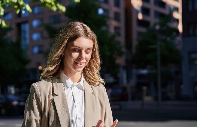 Güneşli bir günde akıllı telefonundan Allianz Türkiye hizmetlerini kullanan gülümseyen genç profesyonel kadın.