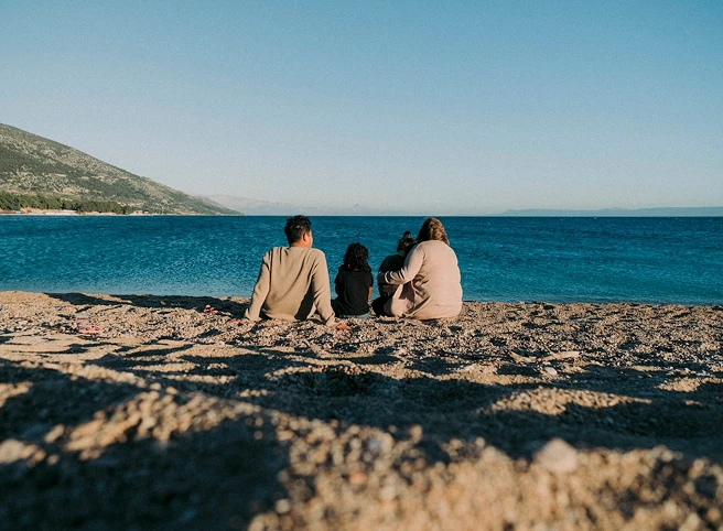Deniz kenarında oturup denizi izleyen dört kişilik aile, Allianz ile huzurlu bir tatil anı.