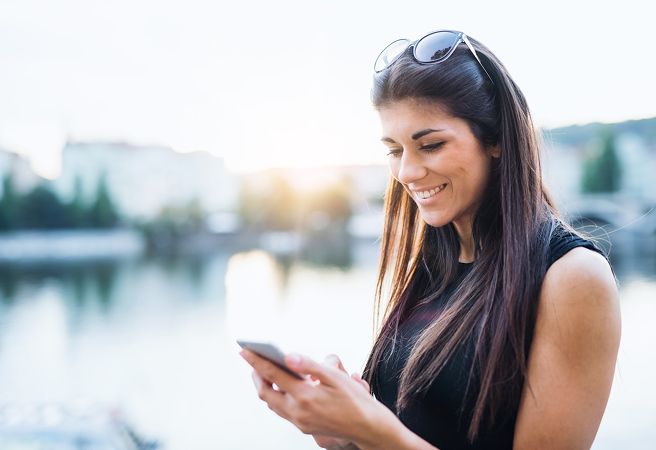 Nehir kenarında gülümseyerek akıllı telefonundan Allianz Türkiye mobil uygulamasını kullanan kadın.