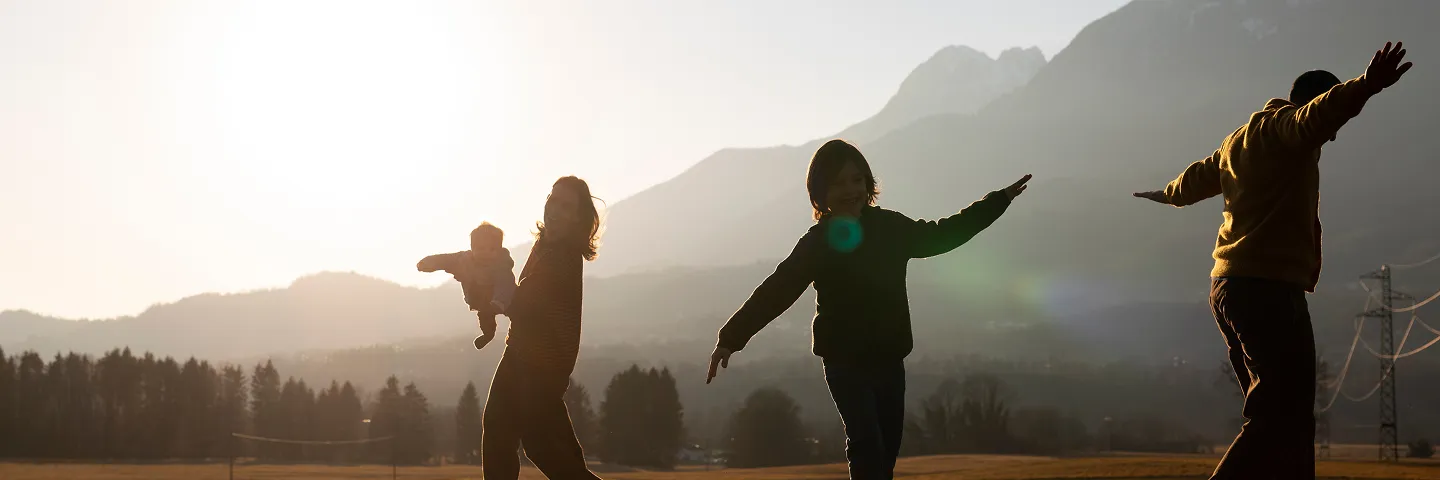Allianz ile güvende hisseden mutlu aile gün batımında dağ manzarasında eğleniyor.