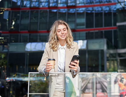 Modern ofis binası önünde elinde kahvesiyle telefondan Allianz sigorta işlemlerine bakan mutlu iş kadını.