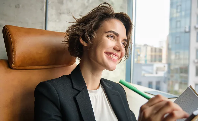 Allianz Türkiye ofisinde pencereye bakarak gülümseyen ve not alan genç kadın çalışan.