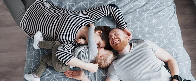 Yatakta sarılan mutlu anne, baba ve küçük çocuk. Hayat ve sağlık sigortası güvencesi.