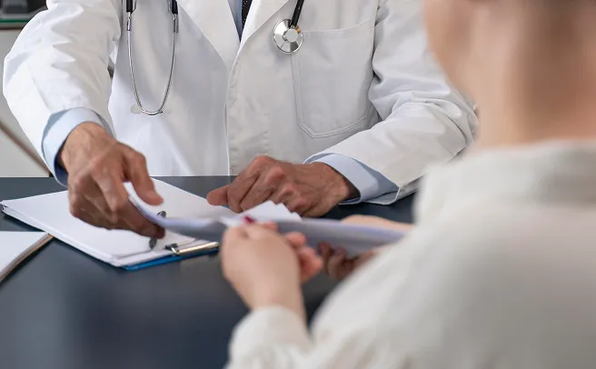 Beyaz önlüklü doktor ve hasta masada sağlık raporlarını inceliyor
