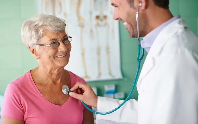 Allianz sağlık sigortası güvencesiyle steteskopla muayene olan mutlu yaşlı kadın hasta ve doktor.
