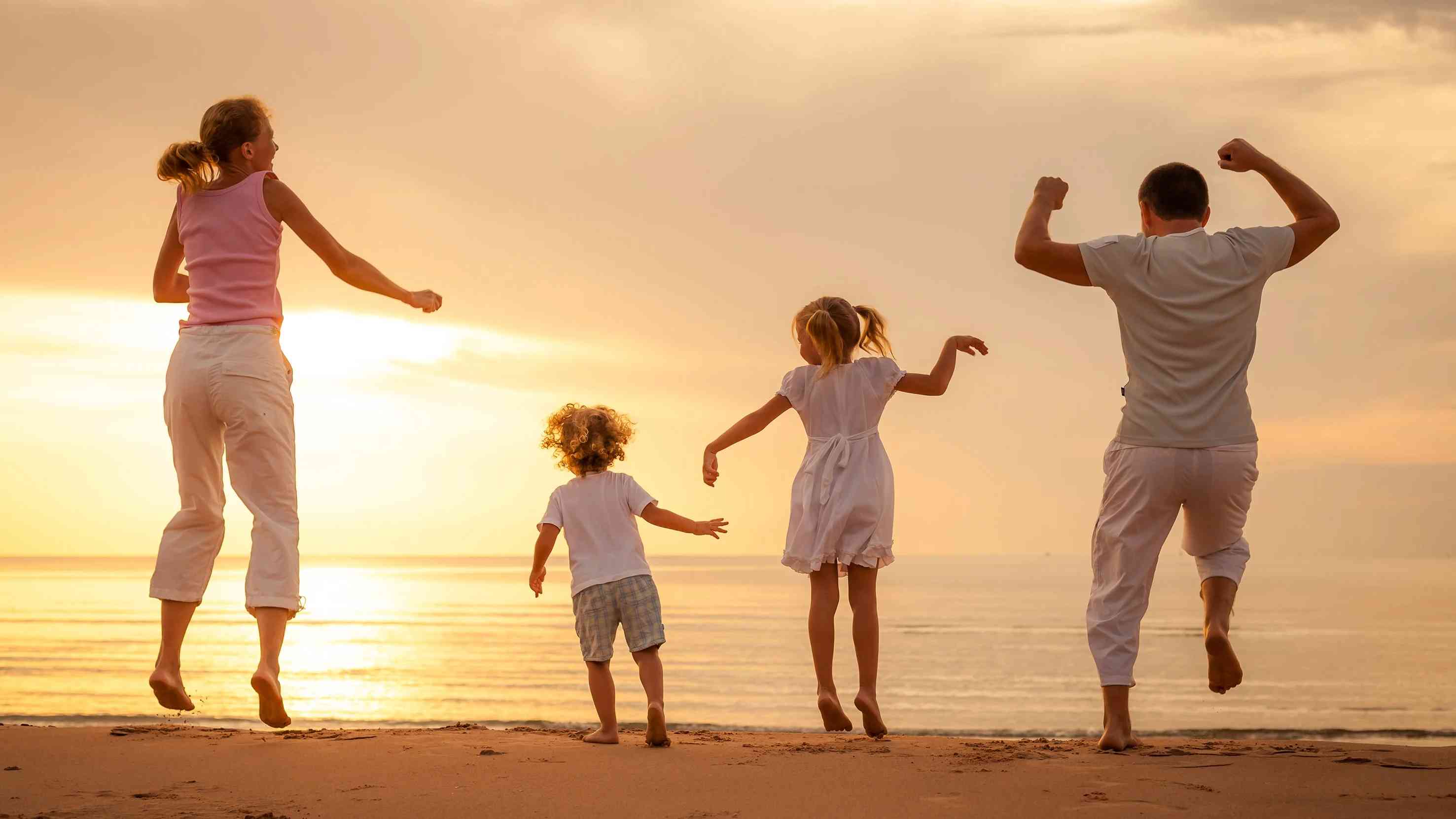 Gün batımında sahilde denize karşı neşeyle zıplayan dört kişilik mutlu bir aile, tatil keyfi yaşıyor.
