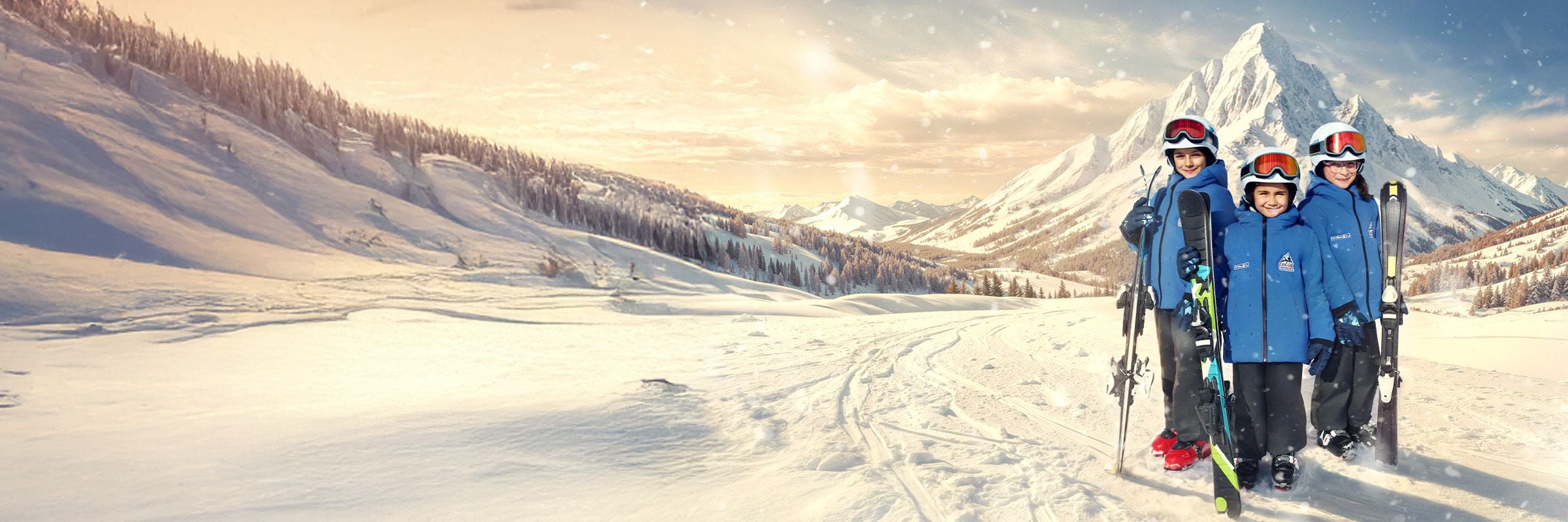 Karlı dağ manzarasında mavi kayak kıyafetleri ve kasklarıyla gülümseyen üç çocuk.