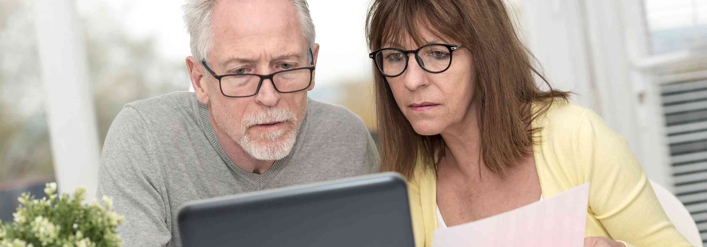 Emekli çift laptopta Allianz sigorta poliçelerini inceliyor, finansal planlama yapıyor.